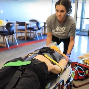 A student moves a mannequin on a stretcher.
